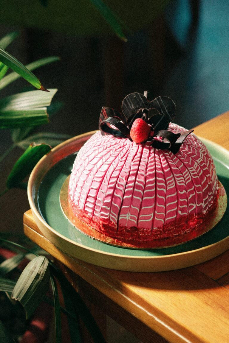 A beautifully decorated pink dome cake with a chocolate flower and cherry garnish, perfect for celebrations.