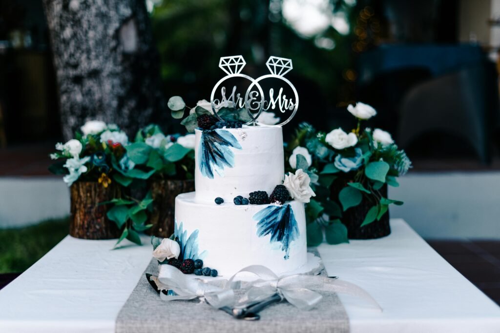 A white wedding cake decorated with blueberries and floral accents, perfect for outdoor celebrations.